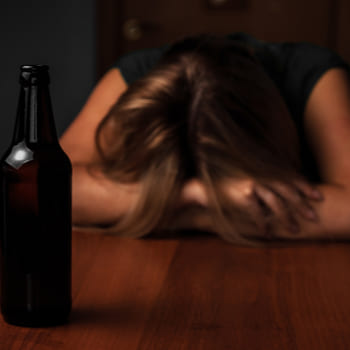 Девушка лежит лицом на столе перед темной бутылкой