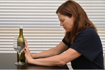 Женщина отодвигает бокал и бутылку